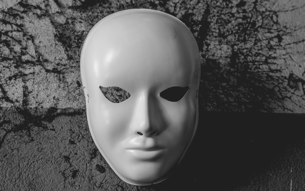 This is a porcelain white mask against a scratch grey surface which is split with two tones of grey with haphazardly drawn black markings. The top section of the surface is a soft grey and the bottom part of the surface is a dark shade of grey. This picture captures the general ill air of "Barry".