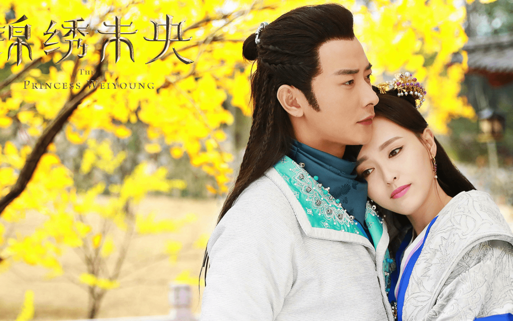This is a cover poster of "The Princess Weiyoung" The leads are hugging towards the right of the camera. It features, green-ish, yellow-ish trees to the left of them, in the background. 