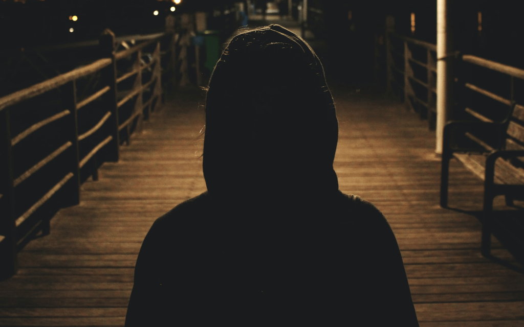 This is a figure of a hooded person on a dock near a body of water at night. This represents the stranger. 
