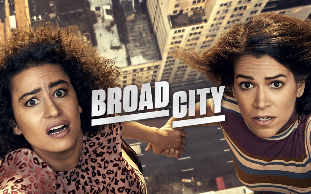 This is a promotional graphic of Ilana Glazer and Abbi Jacobson against the edge of building holding on to each other. Broad City is written between the woman.