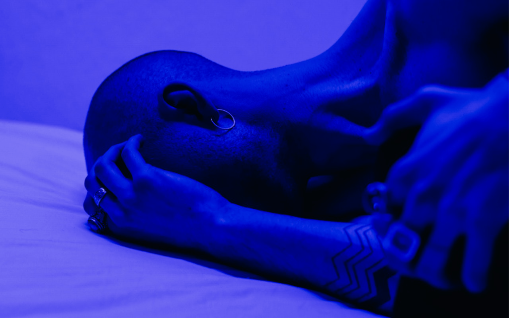 This is a woman covering her face with one had on a bed in a room lit with blue-ish violet light, representing the distress in Grownish- season 3 episode 4.