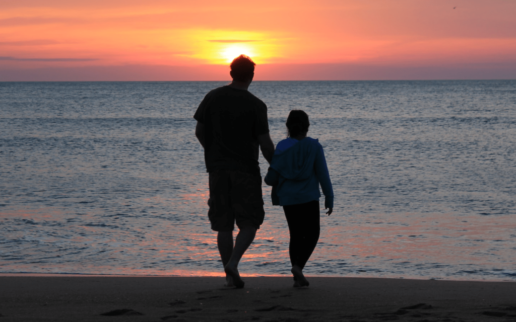 This is a man and a child walking on a beach by the ocean with the sunset behind them. The man and child are shadowed and indistinguishable. This is used to represent Michael and his son in "Road to Perdition".