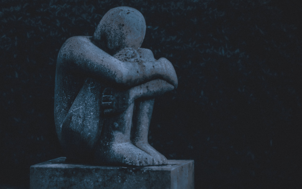 This is a statue of a child sitting with their knees to their chest and their hands wrapped around their calves in sadness. The image seems to have been taken at night. It represents Pearl and Mia's victimization in "Little Fires Everywhere".