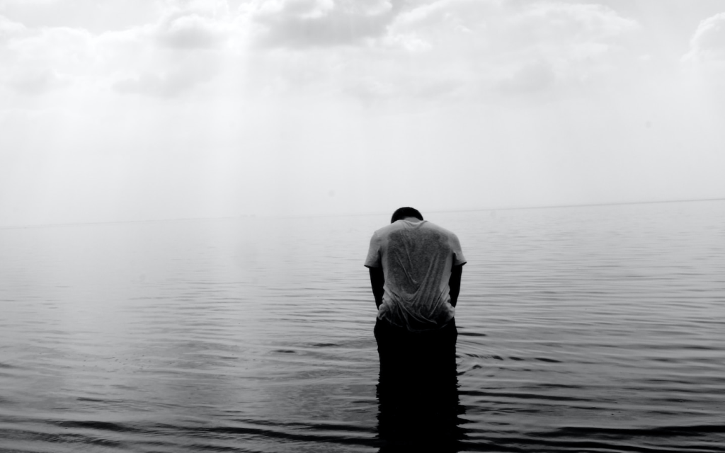 This is a white and black image of a man in a body of water in a wet T-shirt with their back towards the camera, signifying the sorrow in episodes 11 and 12 of "Mr. Queen".