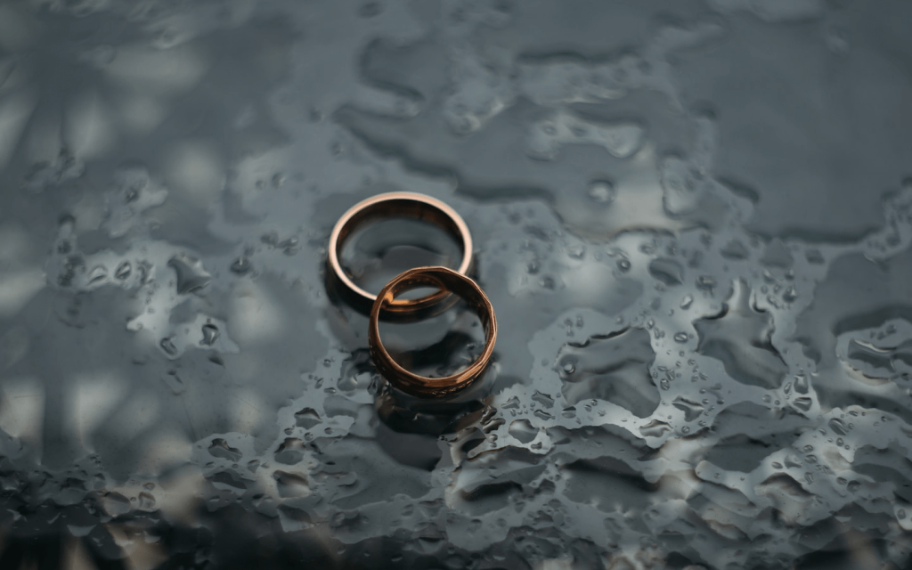 This is two gold rings on a greyed glass-like surface with rain water used to represent the marriage of Joan and Joe in "The Wife".